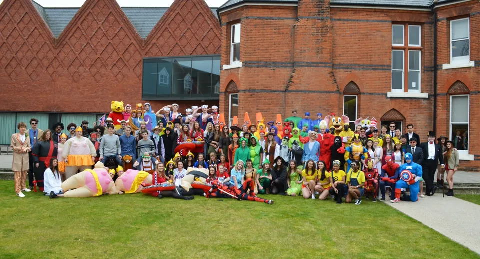 Un gruppo di studenti della Brentwood School in costumi colorati si raccoglie davanti a un edificio storico in mattoni.