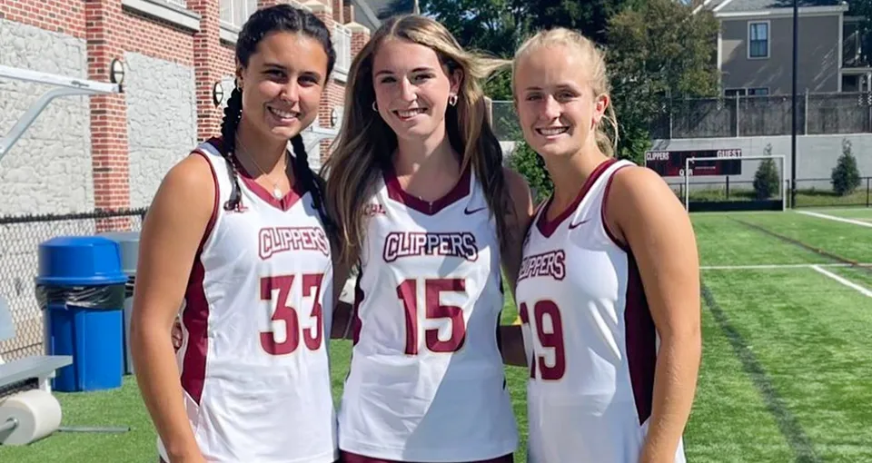 Tre studentesse della Newburyport High School indossano la maglia sportiva della squadra Clippers, in piedi su un prato davanti a un edificio in mattoni.
