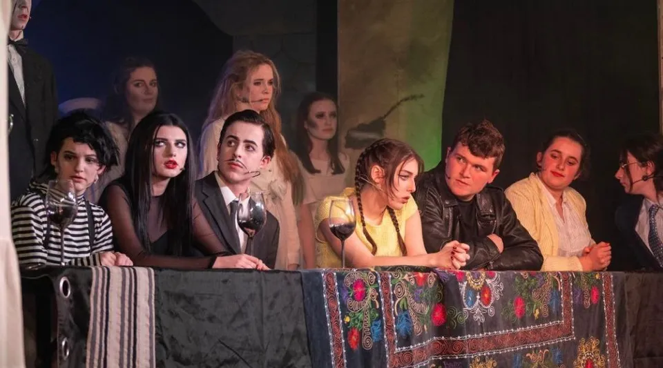 Un gruppo di studenti e studentesse sta su un palco davanti a una scenografia colorata nel campus del Colaiste Muire Cobh.
