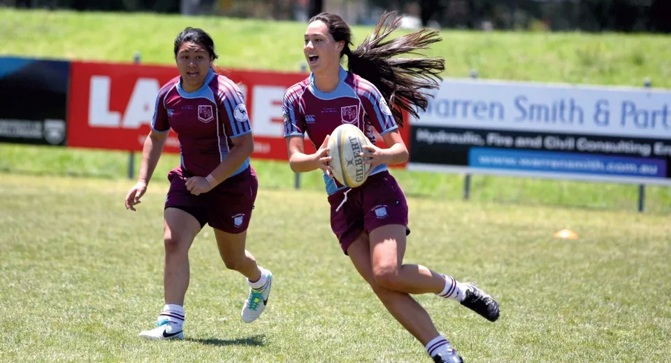 Due giocatrici di rugby in divisa bordeaux corrono sul campo della Clarence High School.