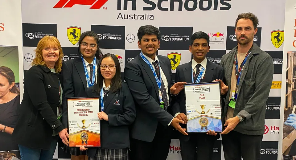 Studenti e adulti della The Heights School sono insieme alla cerimonia di premiazione di F1 in Schools davanti a uno sfondo con logo.