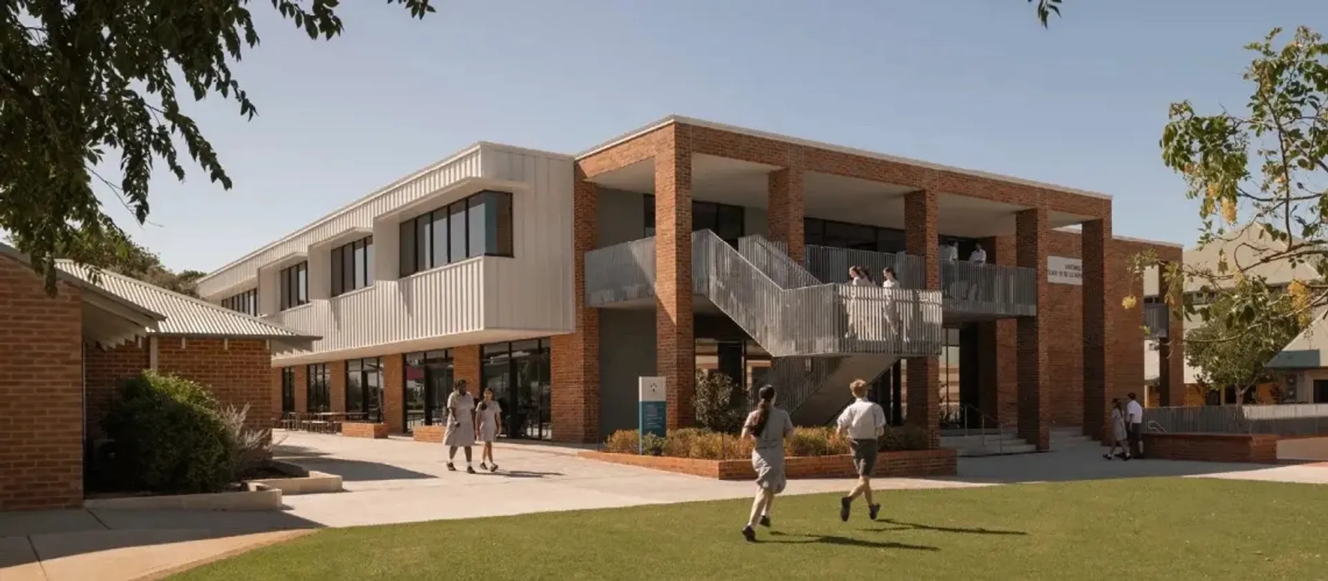 L'edificio moderno della John Septimus Roe Anglican Community School con colonne in mattoni e studenti nel campus.