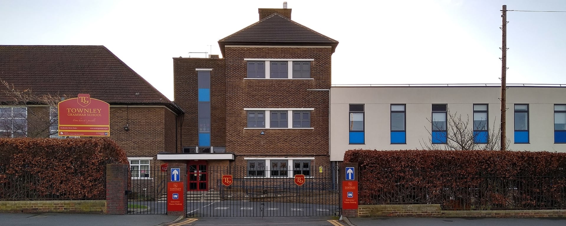Das moderne Gebäude mit dreieckigem Dach auf dem Campus der Townley Grammar School ist von Bäumen und einem gepflasterten Bereich umgeben.