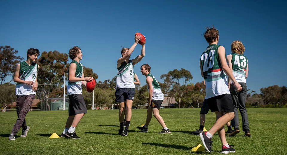 Un gruppo di studenti gioca ad Australian Football sul campo sportivo della Blackwood High School sotto un cielo limpido.