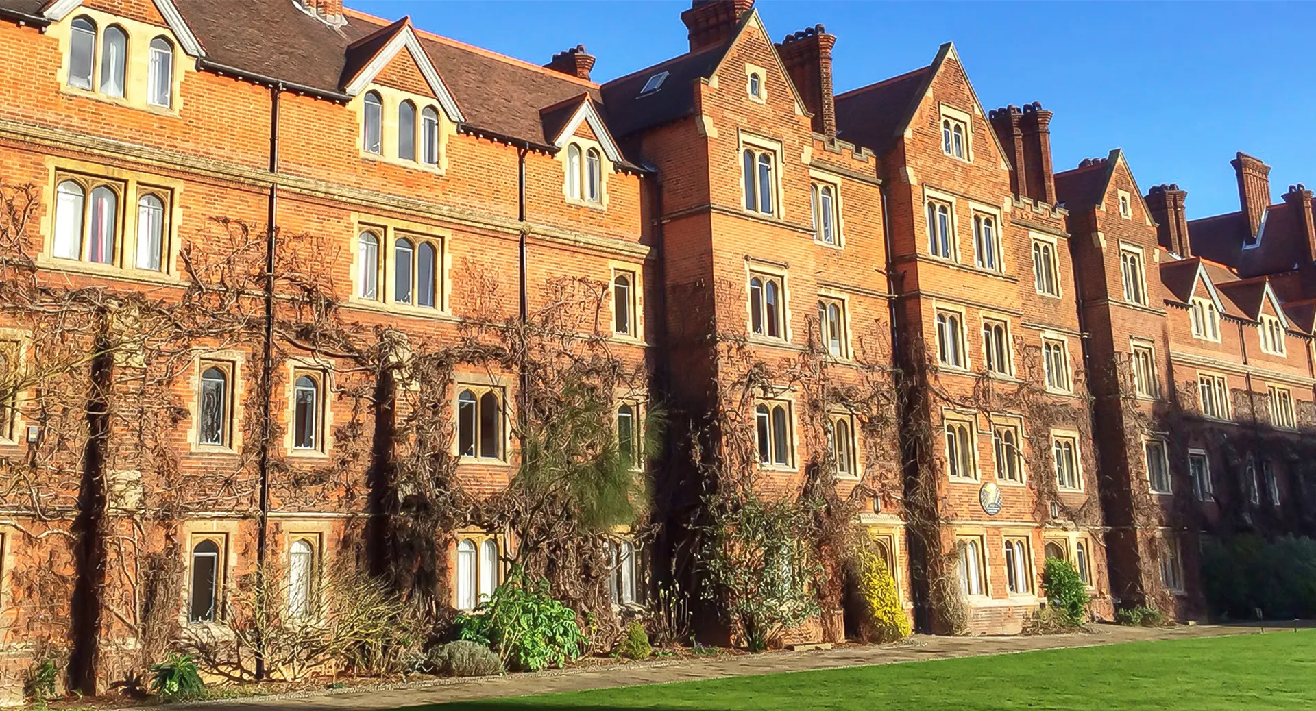 Un edificio in mattoni a più piani del Selwyn College con tetti a due falde e un prato antistante.