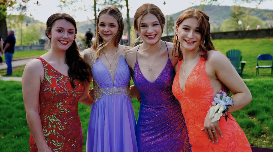 Quattro studentesse della Lake George Junior-Senior High School stanno insieme in abiti colorati su un prato con alberi sullo sfondo.