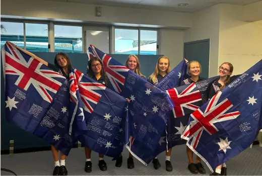 Sechs Schülerinnen halten unterschriebene australische Flaggen in einem Raum hoch