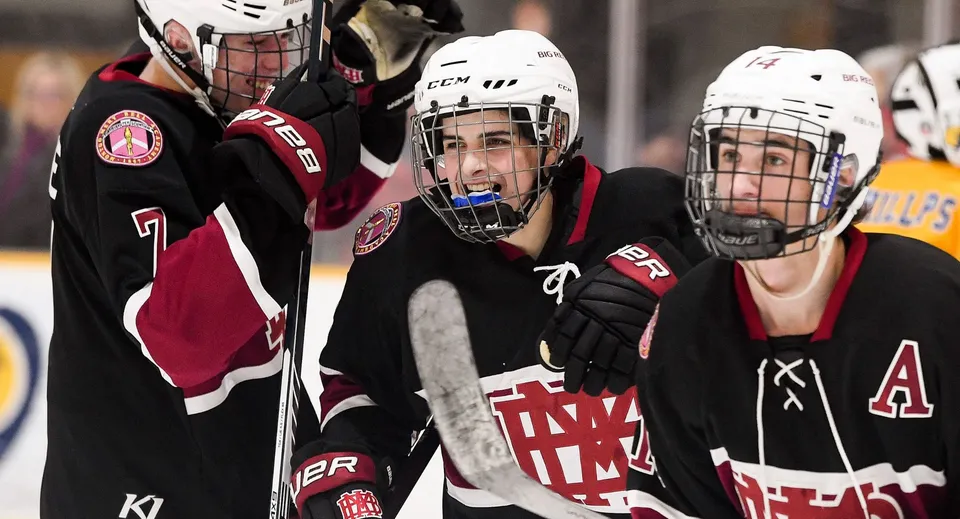 Tre giocatori di hockey su ghiaccio in divisa sul ghiaccio, uno indossa una maglia con le lettere A e M, sul campo da ghiaccio della Royal Vale High School.