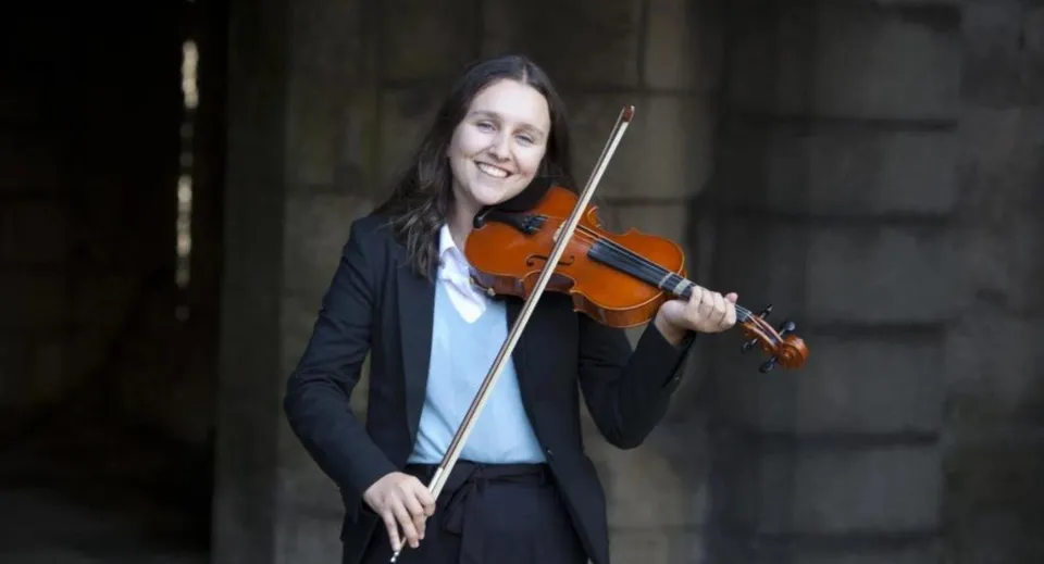 Una persona suona il violino nel campus del King William's College su uno sfondo scuro.