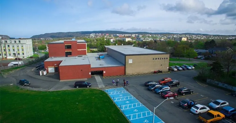 Edificio della Queen Elizabeth Regional High con parcheggio in primo piano e zona residenziale con montagne sullo sfondo.