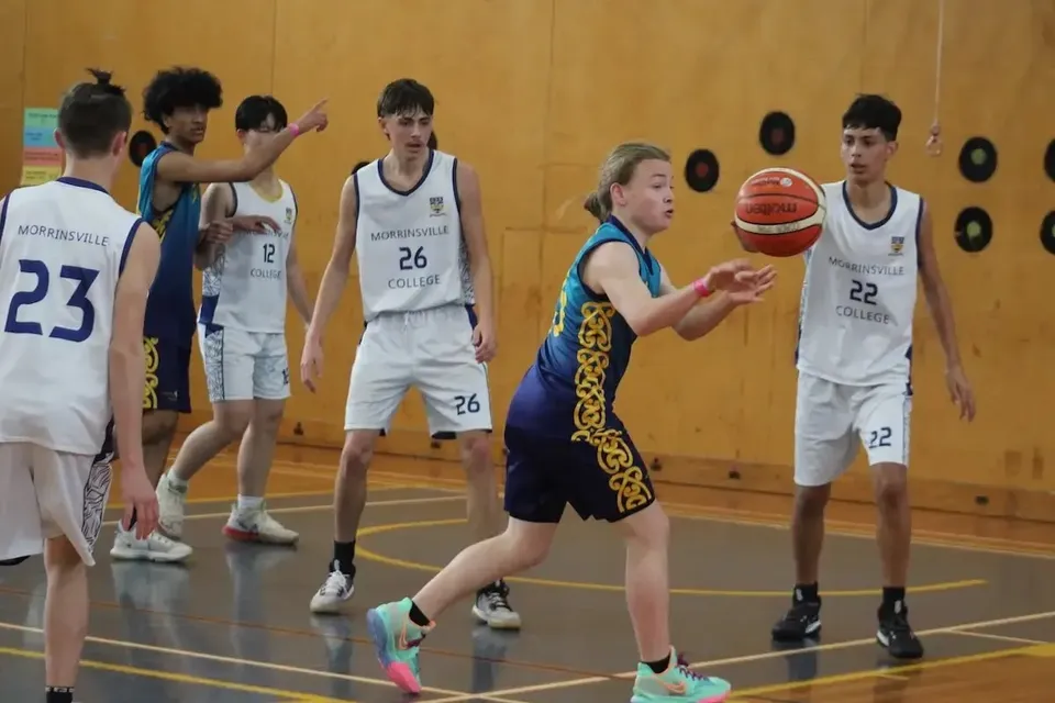 Studenti della Rotorua Lakes High School giocano a basket nella palestra con pareti in legno e decorazioni sullo sfondo.