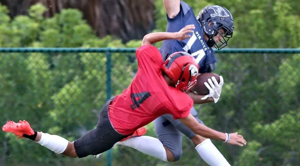 Un giocatore di football in maglia rossa afferra la palla sul campo da gioco della Saint Edward's School.