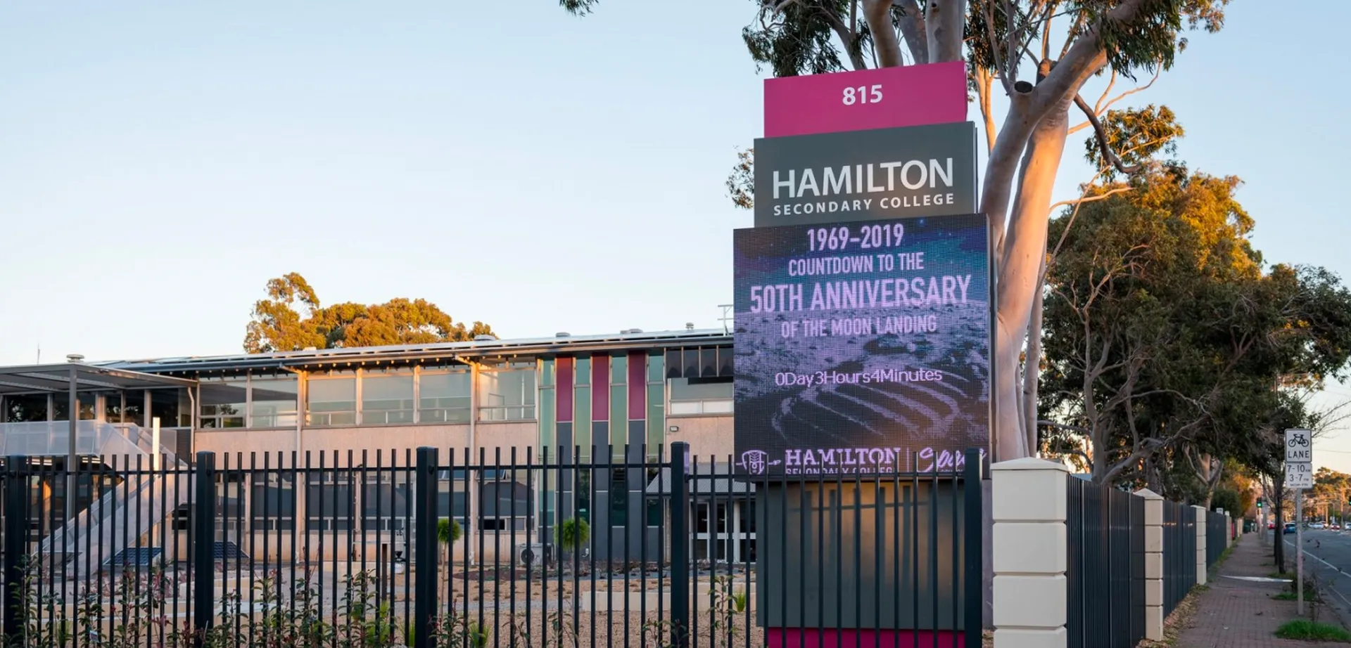 L'ingresso del Hamilton Secondary College con un grande cartello per il 50° anniversario e palme sullo sfondo.