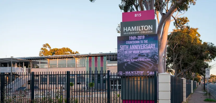 L'ingresso del Hamilton Secondary College con un grande cartello per il 50° anniversario e palme sullo sfondo.
