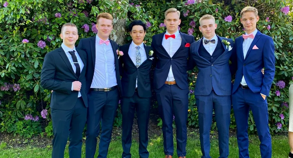 Un gruppo di studenti del Rice College si trova in un giardino verde con fiori in sboccio.