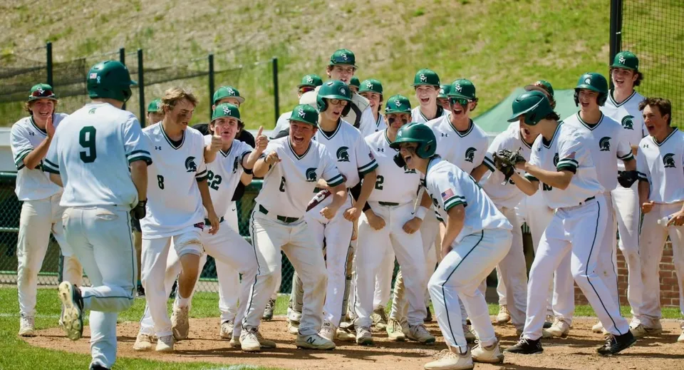 Un gruppo di giocatori di baseball in divisa bianca e caschi verdi sul campo da baseball della St. Mark High School.