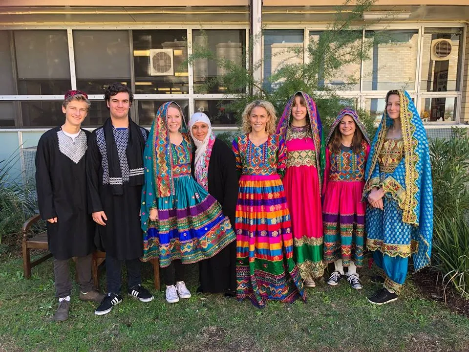 Un gruppo di donne in abiti tradizionali e colorati si trova davanti a un edificio del campus della Pittwater High School.