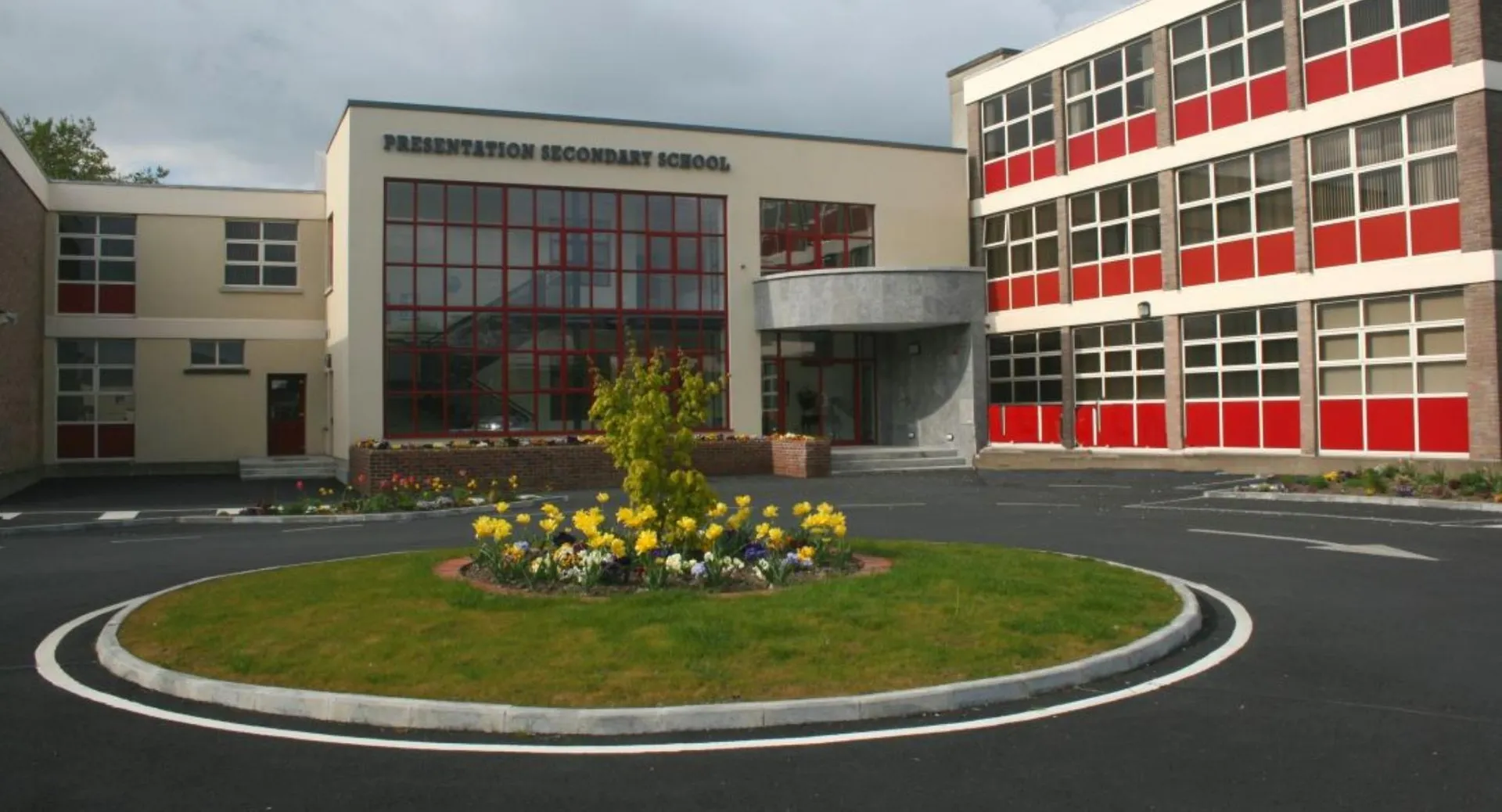 L'edificio moderno a più piani della Presentation Secondary School a Tipperary con grandi finestre e un'aiuola rotonda in primo piano.