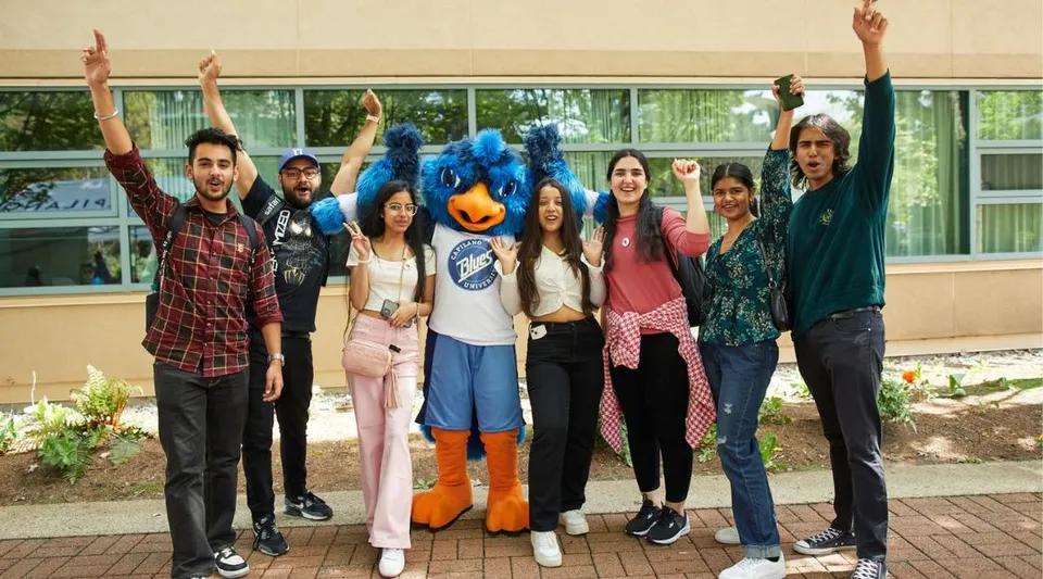 Un gruppo di giovani sta con le braccia alzate davanti a un edificio del campus della Capilano University.