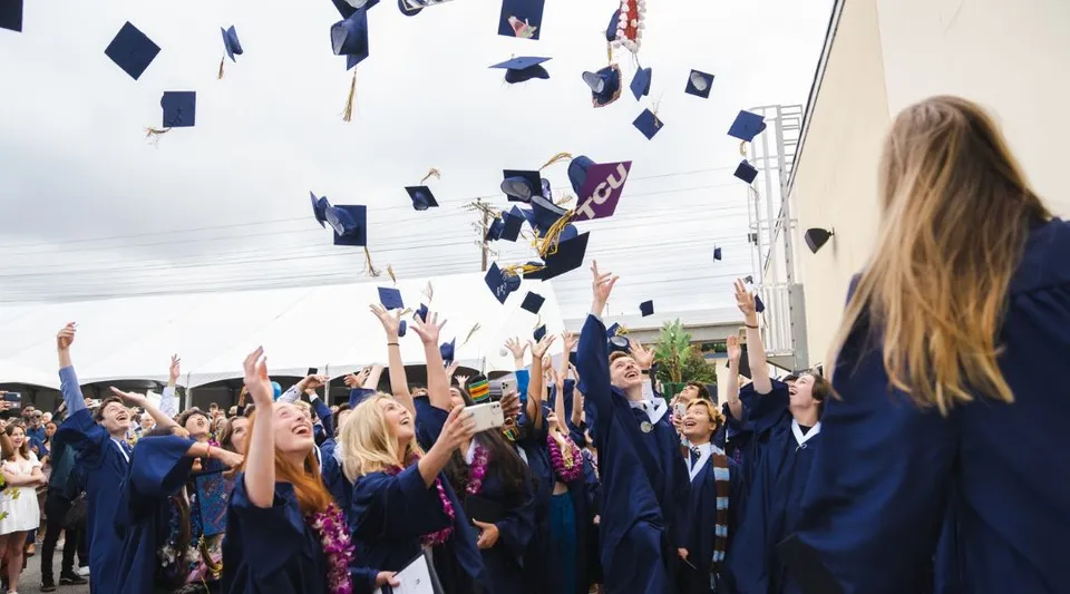 I diplomati della Vistamar School in toga blu lanciano i loro tocchi in aria durante la cerimonia di diploma.