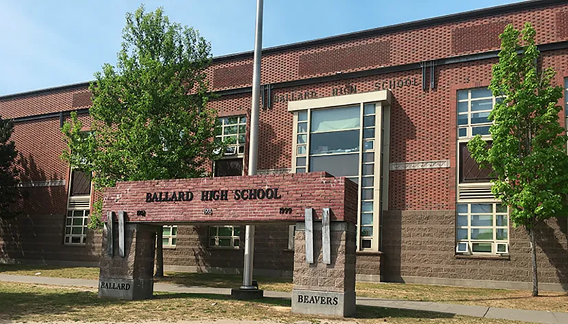 L'edificio in mattoni della Ballard High School è circondato da alberi e lampioni in primo piano.