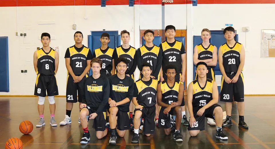 Un gruppo di giovani giocatrici di basket in maglia giallo-nera posa nella palestra della Prince of Wales Secondary School.