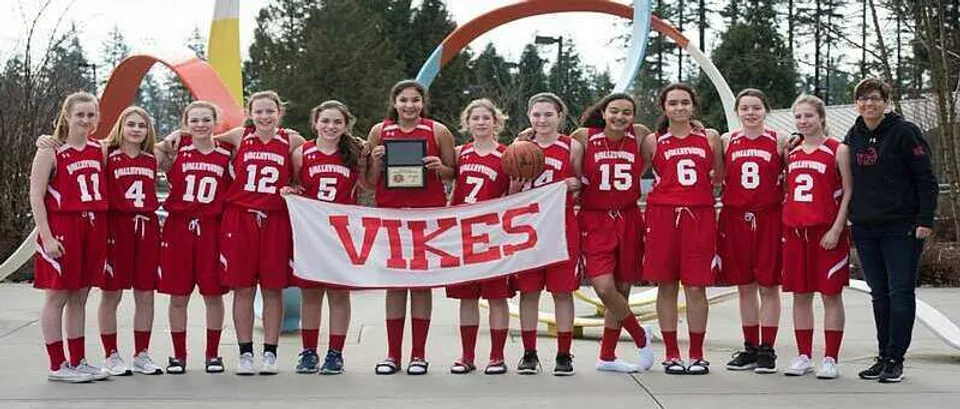 Un gruppo di giovani atlete della Valley View Secondary tiene uno striscione dei Vikes davanti a un arco colorato all'aperto.