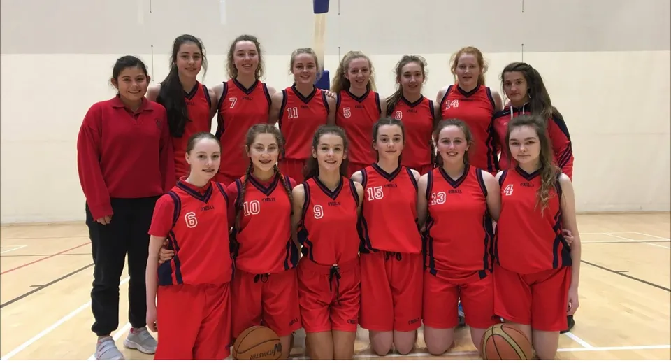 Studentesse della Presentation Secondary School (Cork) sono insieme in palestra con le loro maglie da basket rosse.
