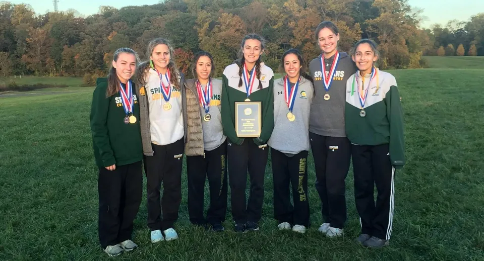 Un gruppo di giovani atlete della St. Peter High School sta in piedi con le medaglie su un campo d'erba davanti agli alberi.