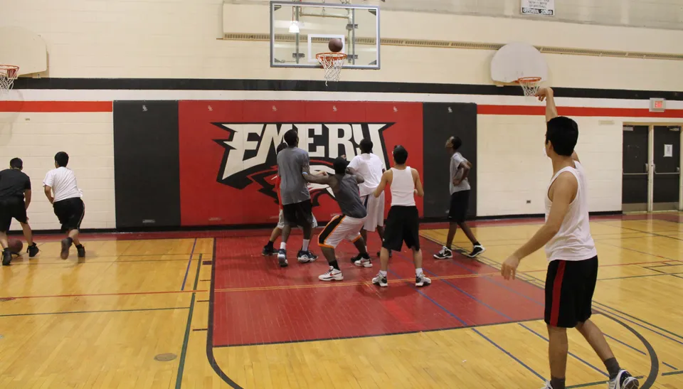 Un gruppo di studenti gioca a basket sul campo sportivo dell'Emery Collegiate Institute davanti a una grande pubblicità di Exert.
