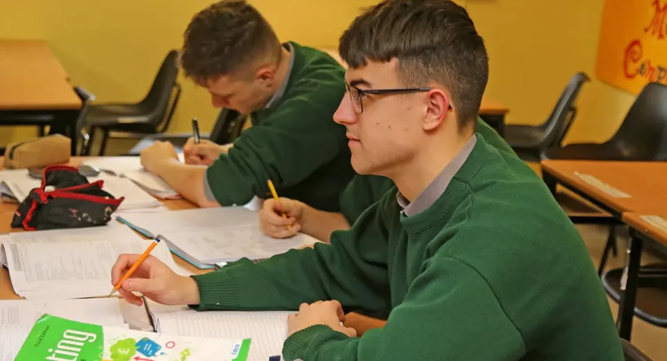 Due studenti in divisa verde siedono concentrati nell'aula della Jesus and Mary Secondary School e lavorano a dei compiti.