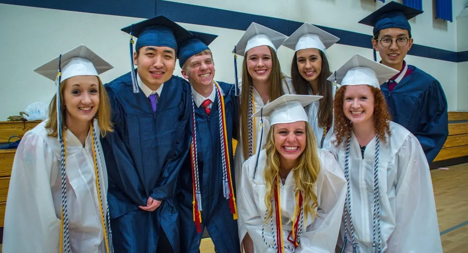 Un gruppo di diplomati e diplomate della St. Francis Xavier High School si trova davanti a una parete blu e bianca.