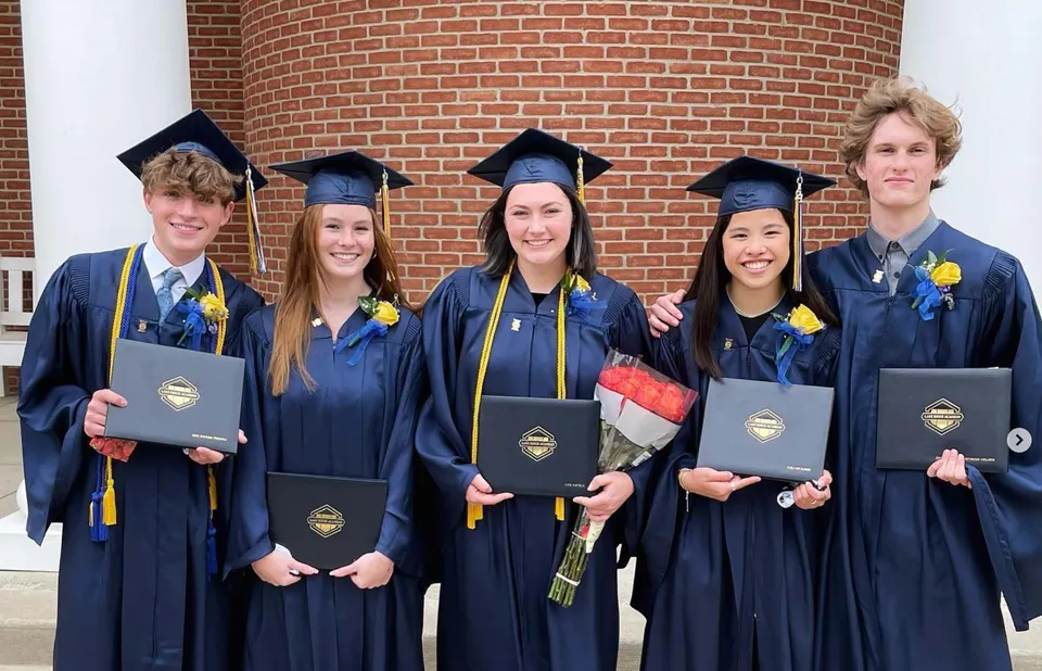 Un gruppo di cinque diplomati della Lake Ridge Academy davanti a un muro di mattoni con i loro diplomi in mano.