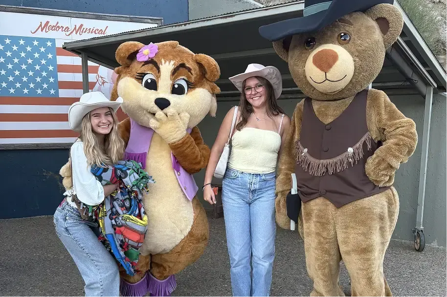 Dos estudiantes con sombrero de vaquero posan con dos mascotas en el Medora Musical