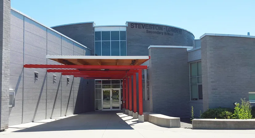 L'edificio a più piani della Steveston-London Secondary School mostra un ingresso rosso con grandi finestre e un piazzale esterno pavimentato.