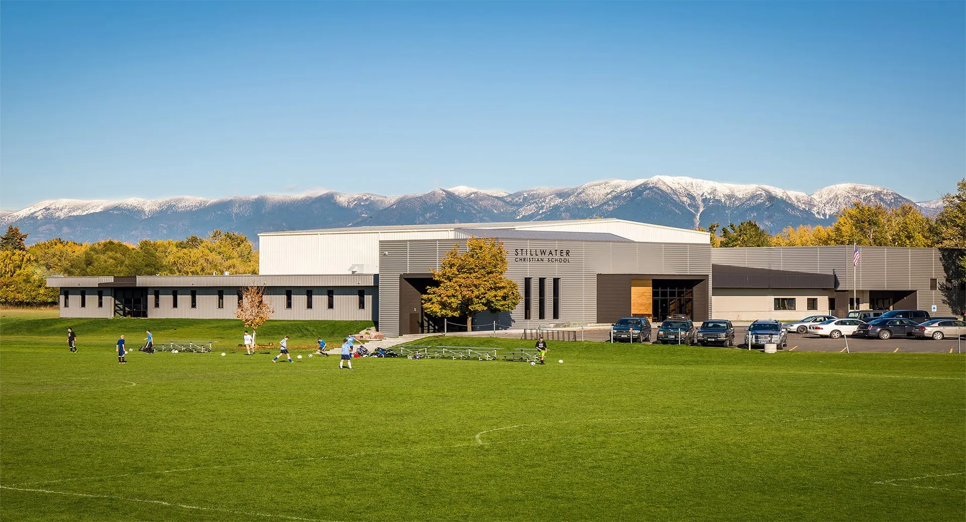 L'edificio moderno a più piani della Stillwater Christian School si trova davanti a un grande parcheggio e a un prato con montagne innevate sullo sfondo.