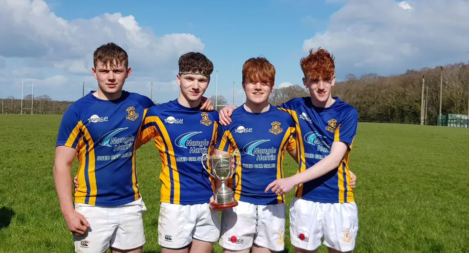 Quattro studenti del St. Michael's College in divisa sportiva tengono insieme un trofeo su un campo.