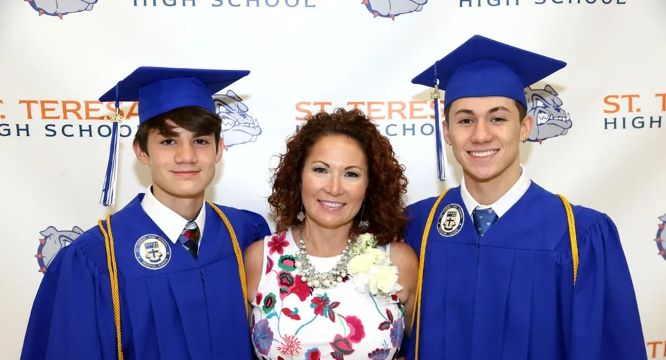 Tre studenti della St. Mother Teresa High School indossano l'abito da diploma davanti a uno sfondo con la scritta High School.