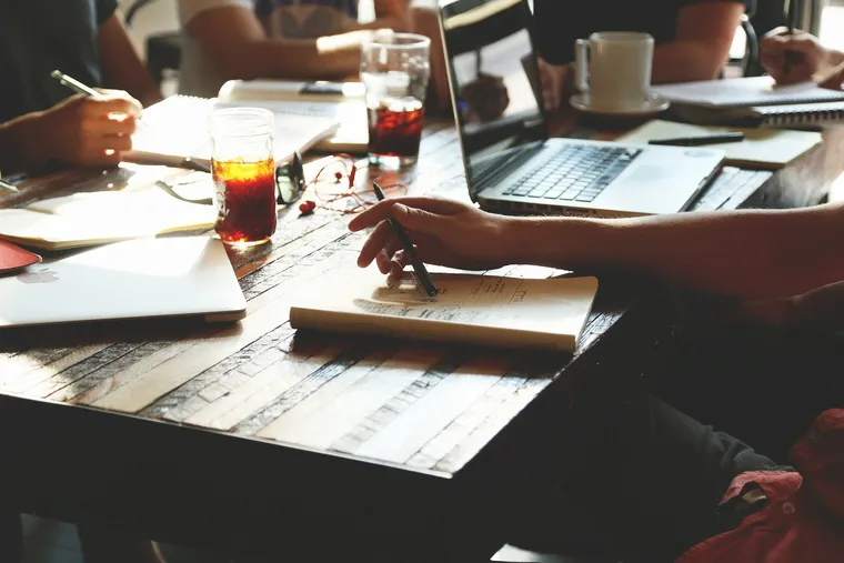 Mehrere Personen arbeiten mit Notizbüchern, Laptops und Getränken an einem Holztisch
