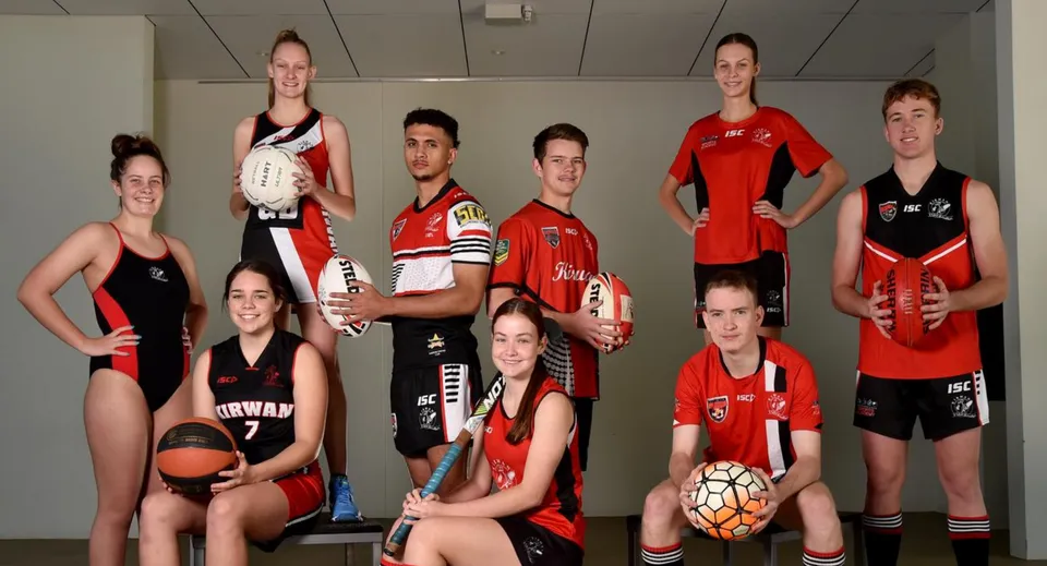 Un gruppo di giovani atleti della Kirwan State High School posa in palestra con le divise della squadra e attrezzi sportivi.
