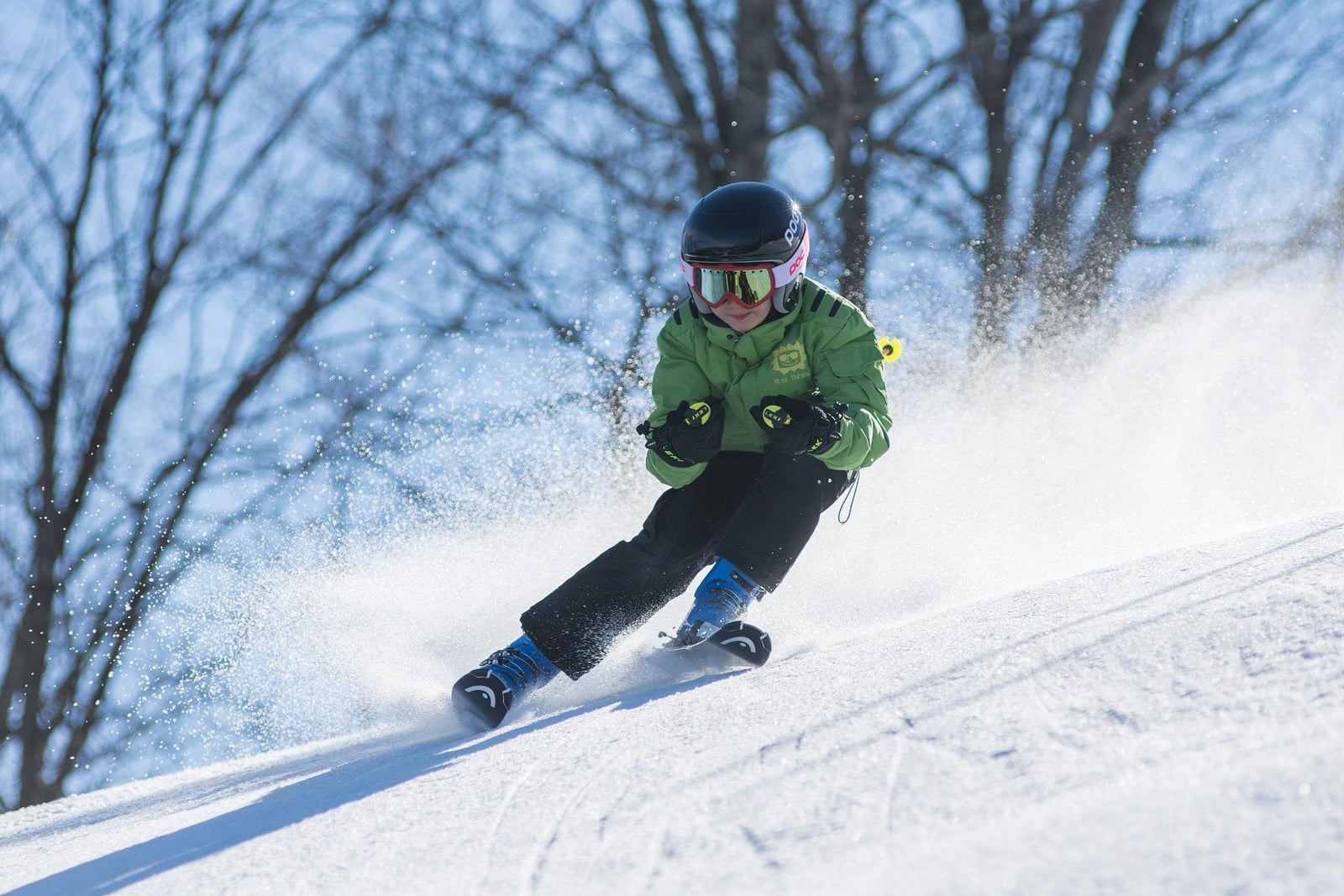 Kind mit Helm und Skibrille fährt Ski auf einer verschneiten Piste