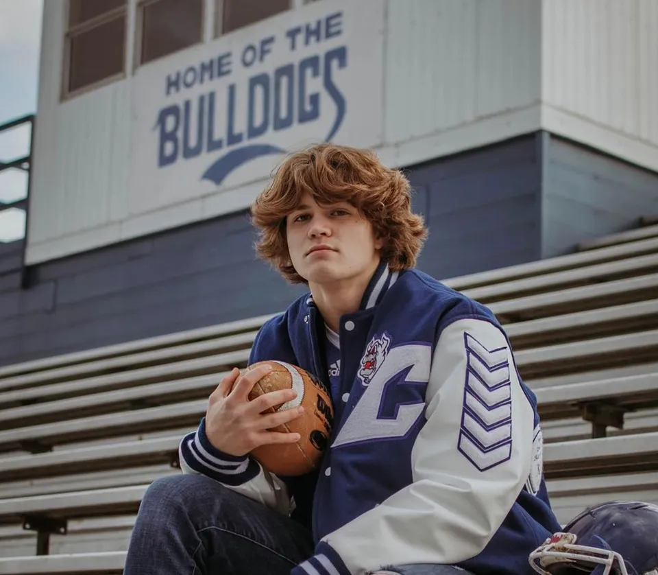 Uno studente della Centerville Senior High School sta in piedi con un pallone da football davanti a un edificio con la scritta Bulldogs.