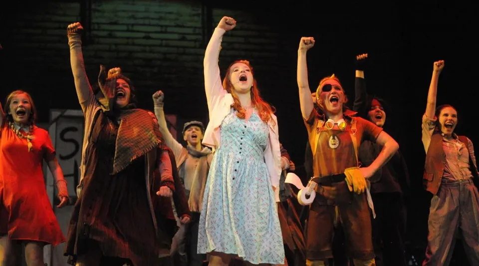 Studenti dell'Ashland School District mettono in scena uno spettacolo teatrale su un palco con luci soffuse.