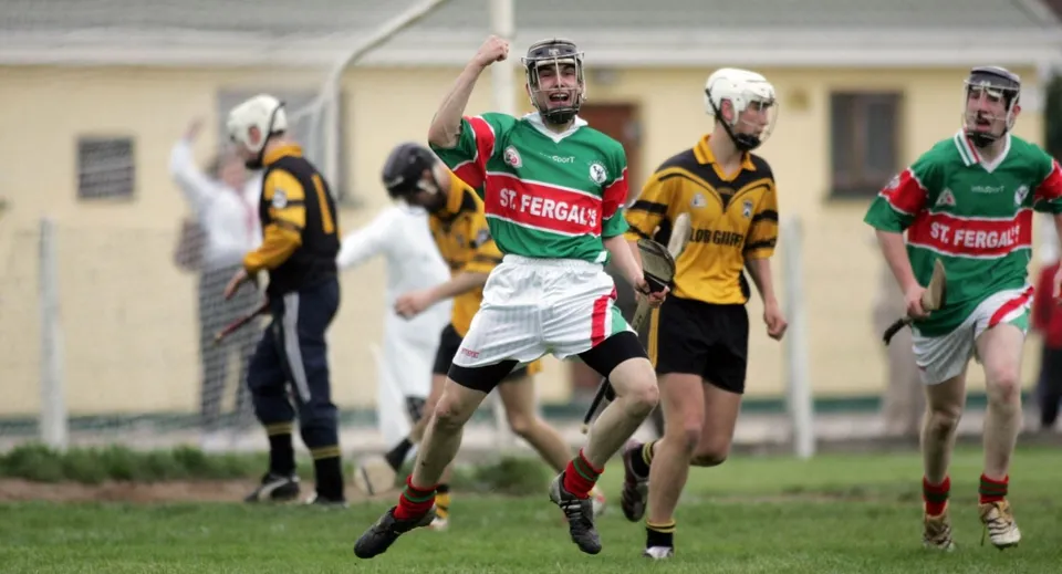 Un gruppo di studenti gioca a Hurling sul campo sportivo del St. Fergal’s College con edifici sullo sfondo.