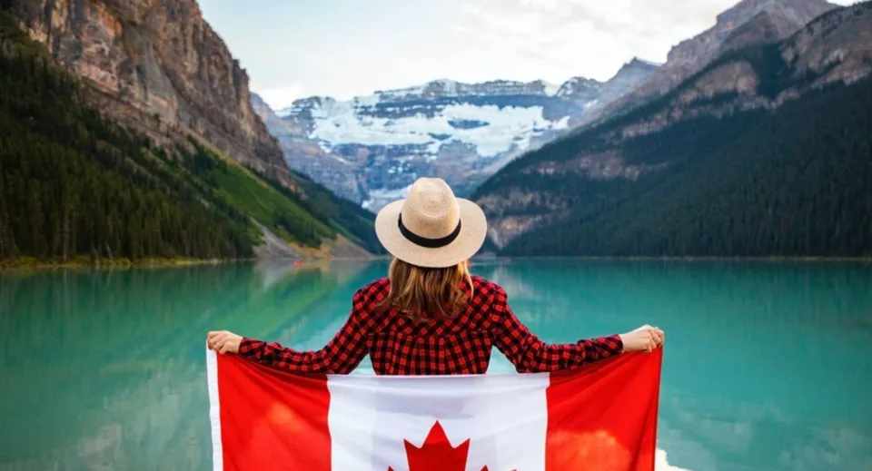 Una persona davanti a un lago turchese con montagne innevate nel terreno della John McCrae Secondary School.