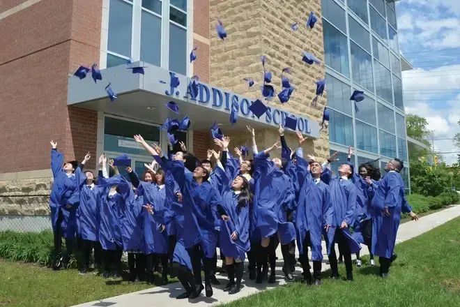 Un grupo de graduados de J. Addison School celebra sus logros académicos frente a un edificio de ladrillo.