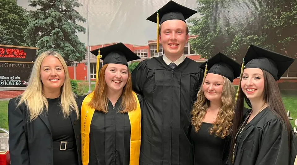 Un gruppo di cinque diplomati si trova davanti all'edificio della South Grenville District High School e festeggia il proprio diploma.