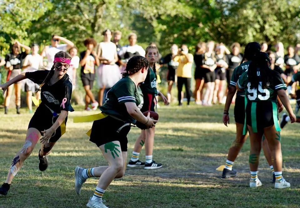 Un gruppo di studenti della Indian River Charter High School si riunisce su un campo sportivo circondato da alberi.