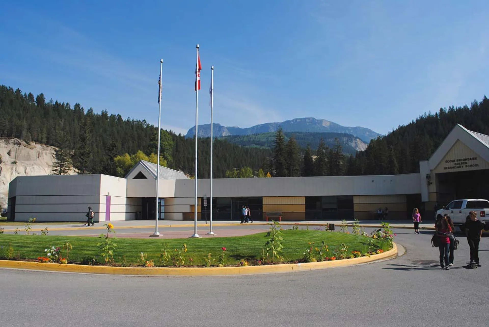 L'edificio moderno a più piani della Golden Secondary School, con le bandiere sul tetto, sorge davanti a montagne coperte di boschi e a un prato ben curato.