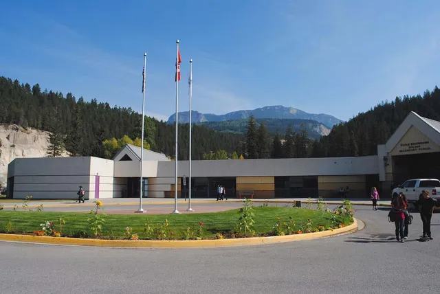 El moderno edificio de varios pisos de la Golden Secondary School con banderas en el tejado se encuentra ante montañas boscosas y un césped bien cuidado.